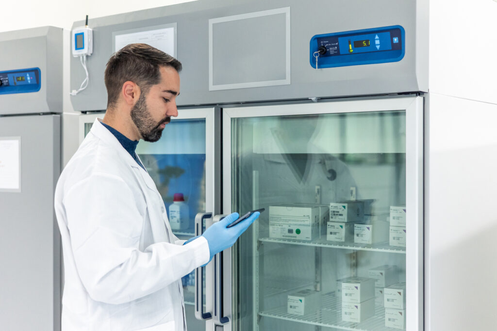 Scientist using a digital tablet near a laboratory refrigerator storing medical samples